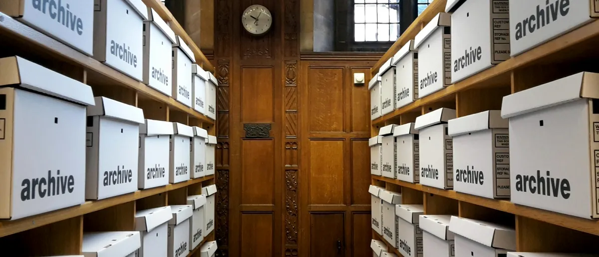 Rows of white archive boxes on wooden shelves in a records room